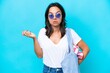© luismolinero - Young caucasian woman holding a beach bag isolated on blue background having doubts while raising hands