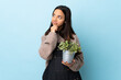 © luismolinero - Young brunette mixed race woman holding a plant over isolated blue background having doubts and with confuse face expression.
