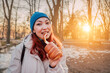 © EdNurg - Young woman in warm clothes enjoying a traditional Trdelnik sweet pastry in a park at golden hour during winter travel