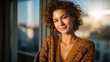 © Maksym - Portrait of a confident curly-haired woman smiling warmly near a bright window, sunlight creating soft highlights and golden reflections in her hair
