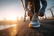 © Arnaud - Athlete tying running shoes on bridge at sunrise with city skyline in background, motivation and focus concept.