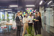 © Studio Romantic - Group of business professionals collaborating in modern office, brainstorming ideas with sticky notes on glass wall. Smiling team of colleagues discussing strategies, showing teamwork and creativity.