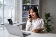 © Wasana - Asian businesswoman talking on phone and working on laptop in modern office
