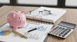 © Heri - Piggy bank, calculator, and documents on a wooden desk representing financial planning and savings for an emergency fund