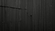 © Nurmadinah - Vertical ridged black metal paneling with dents and scratches, creating a textured industrial surface look
