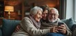 © Maryna - Elderly couple with adult daughter sitting on sofa at home. Senior man, woman in knitwear using smartphone together. Happy family video calling on mobile phone. Smiling old people hugging, looking at