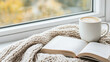 © siraphol - Cozy scene with open book and cup of latte on knitted blanket by window, inviting relaxation and warmth