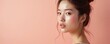 © Maryna - Young Asian woman with glowing skin and soft makeup. She has her hair up in a bun. The background is a soft peach color, creating a gentle aesthetic. Her makeup includes subtle blush and lip color.