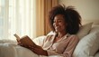 © Maryna - Young black woman happily reads book in cozy bed. Smiling, relaxed person enjoys morning routine with sunlight and soft pillows. She is learning a new story or information.