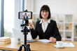 © sofiko14 - Caucasian woman wearing black suit recording video blog in office environment using smartphone on tripod
