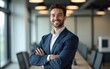 © Samuel - Smiling young businessman standing with his arms crossed at work. High quality