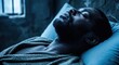 © vadosloginov - Man resting peacefully on a bed in a dimly lit room with dark blue tones at night