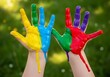 © IQ-Photography - Child's hands covered in vibrant paint against a blurred green background in a playful display of color