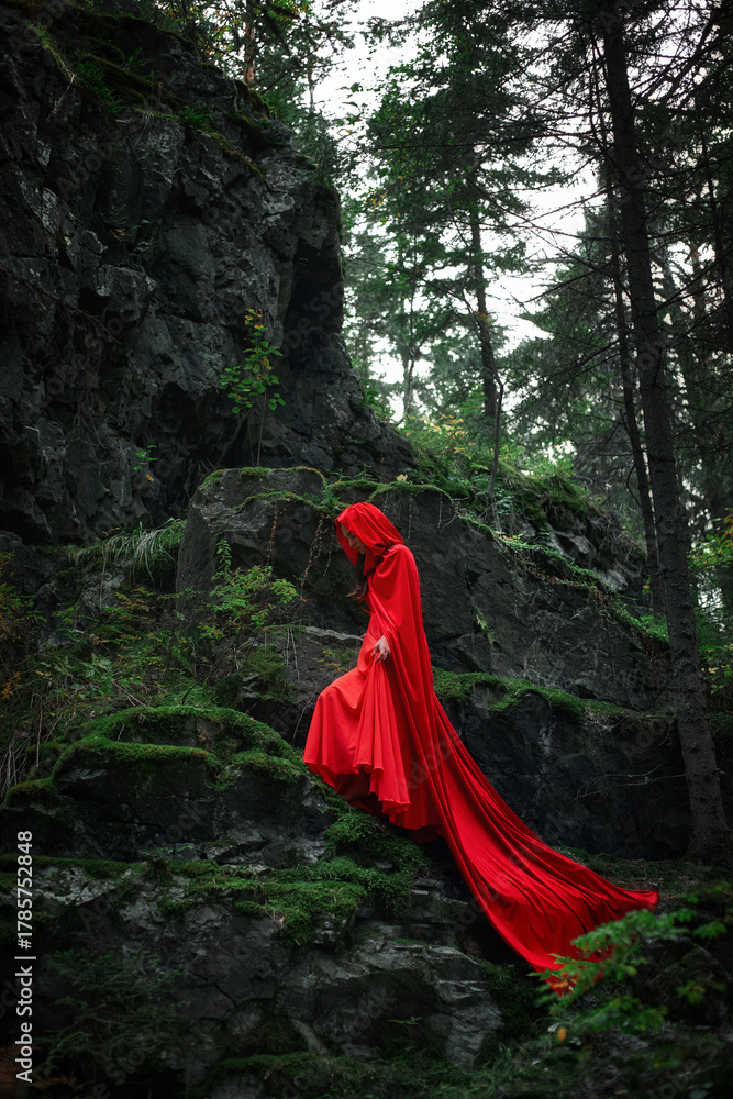woman wearing a long red cloak gracefully walks down a rocky path ...