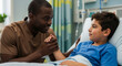 © OlgaNeuroArt - Male nurse comforting a young boy patient in a hospital bed. Caring Black healthcare professional holding a child's hand for support. Pediatric medical care and compassion