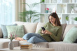 © PheelingsMedia - Happy woman in green using smart phone on a couch