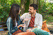 © Srdjan - Young couple cuddling on a park bench, smiling and leaning in for a kiss, sharing an affectionate embrace in sunny green nature casual outfits, warm connection, romantic date outdoors