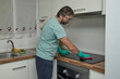 © Anna Baranova - Man cleaning electric stove in modern kitchen with gloves and sponge. Person washing and wiping cooktop with detergent and cloth, doing household chores and keeping kitchen clean. Concept of home