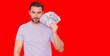 © Volodymyr - Good payment. Handsome man holding money isolated over red studio, banner copy space. Money in dollar banknotes. Pile of cash, finance, investment and money saving. Mockup banner.