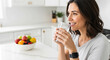 © Atmospheres - Healthy smiling woman drinking a glass of fresh clean water in a modern white kitchen for wellness and hydration.