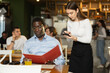 © JackF - African man holds a menu with a choice of food in hands, he asks the waitress about the chef's dish, talks about food preferences and allergies. Client of a European restaurant orders dinner