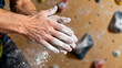 © LI - Close-up of a rock climber dusting their hands with white chalk powder before gripping a hold on an indoor climbing wall.