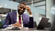 © Prostock-studio - Positive wealthy young black manager working at modern office, sitting at workdesk in front of laptop, taking notes and smiling, panorama with copy space. Business opportunities concept
