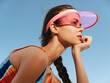 © SHOTPRIME STUDIO - Portrait of a young athletic woman in a pink visor, braided hair, and colorful tank top, gazing toward the distance against a clear blue sky.