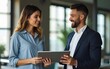 © yuan - Two busy happy diverse professional business team people working in office with digital tablet. Male executive manager talking to female partners having conversation standing at work using tab.