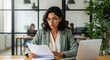 © PRASANNAPIX - Focused businesswoman reading documents at her modern office desk.
