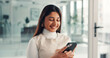 © peopleimages.com - Phone, smile and businesswoman in office with networking, communication or email on mobile app. Happy, technology and female person with cellphone for contact, texting or research online in workplace