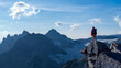 © edb3_16 - Hiker Stands on a Cliff Overlooking Jagged Mountain Range Under Blue Sky During Sunrise Adventure