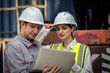 © Thanadon88 - Two people wearing hard hats are looking at a laptop. One of them is a woman. They are looking at a document on the laptop