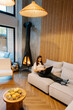 © Doralin - Woman relaxing, working remotely in cozy cabin living room