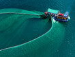 © AmazingAerialAgency - Aerial view of a fishing boat casting a wide net across the shimmering turquoise sea in the bright sunlight, An Ninh Dong, Phu Yen, Vietnam.