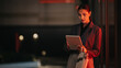 © qunica.com - A poised professional woman stands outdoors at night, examining content on a tablet. The red ambient lighting adds a modern, urban business vibe.