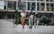 © qunica.com - Two professional women walk across a sleek corporate campus, one holding a tablet and the other with documents.