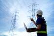 © KANGWANS - A man wearing a hard hat and safety vest is standing in front of a power line
