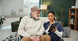 © peopleimages.com - Old man, nurse and tablet with wheelchair in home, talk and review with progress report for recovery. Caregiver, tech and elderly person with disability, feedback or app for rehabilitation in house