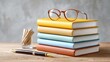 © stardadw007 - A stack of colorful books with glasses on top, a pen, and a glass holder with wooden sticks, arranged neatly on a wooden surface.
