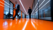 © Curioso.Photography - People walking in modern office corridor with bright orange floor and glass walls.