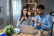 © Srdjan - Couple reviewing household budget at home woman with coffee and tablet, man focused on laptop; paperwork on table in cozy living room, finances, bills, savings, remote work.