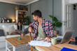 © Srdjan - Man reviews bills at a laptop while his partner relaxes with a tablet on the sofa in a cozy living room. Papers, coffee and tech on the table. Concept: home budgeting, monthly expenses