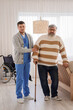 © Pixel-Shot - Young caregiver taking care of senior man with stick at home