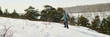 © pressmaster - Caucasian middle aged man hiking through snowy landscape with backpack and snowshoes, moving uphill along trail surrounded by winter forest, facing away from camera