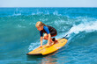 © Tropical studio - Happy young surfer girl with surfboard have fun on beach, riding on small ocean waves. Summer adventures, active families, parents and kids lifestyle, sports activities on school holiday with kids