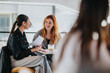 © qunica.com - Two young women share a friendly discussion over papers and coffee in a bright cafe, suggesting teamwork, networking, and casual business meetings in a modern workspace.