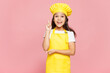 © ViDi Studio - Small kid child girl housewife chef cook baker mother's helper wear yellow apron toque cap holding index finger up with great new idea isolated on pastel plain pink background. Cooking food concept.
