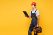 © ViDi Studio - Young employee laborer handyman man wears helmet overall hold clipboard paper account documents toolbox isolated on plain yellow background. Instruments renovation apartment room. Repair home concept.