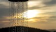 © Rina - Close up of water falling from a shower head against a soft focus sunset sky with golden sunlight filtering through.